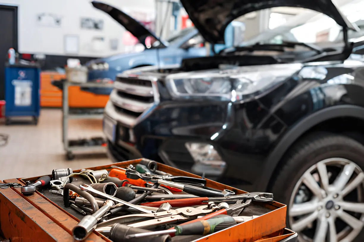 A close-up view of a toolbox filled with various tools, with two cars in the background inside an auto repair shop in Texas.