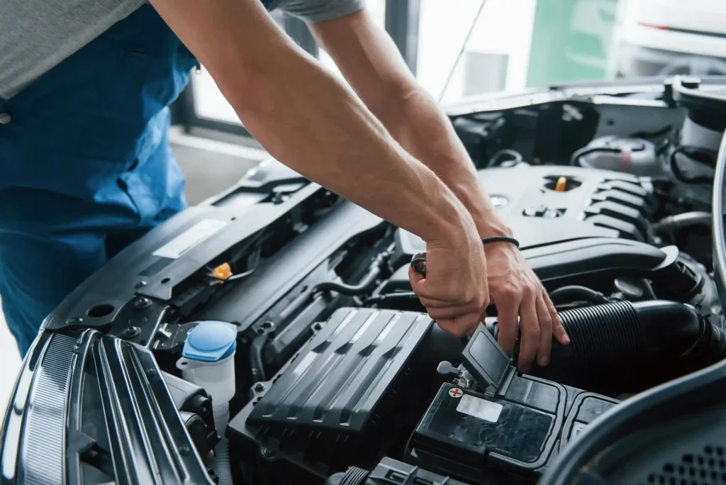 Mechanic in an auto shop repairing a car engine under the hood in Sugar Land, Texas.