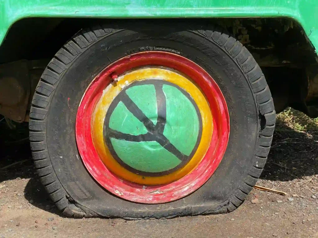 A green truck with a flat tire, showing significant damage and an uneven shape.