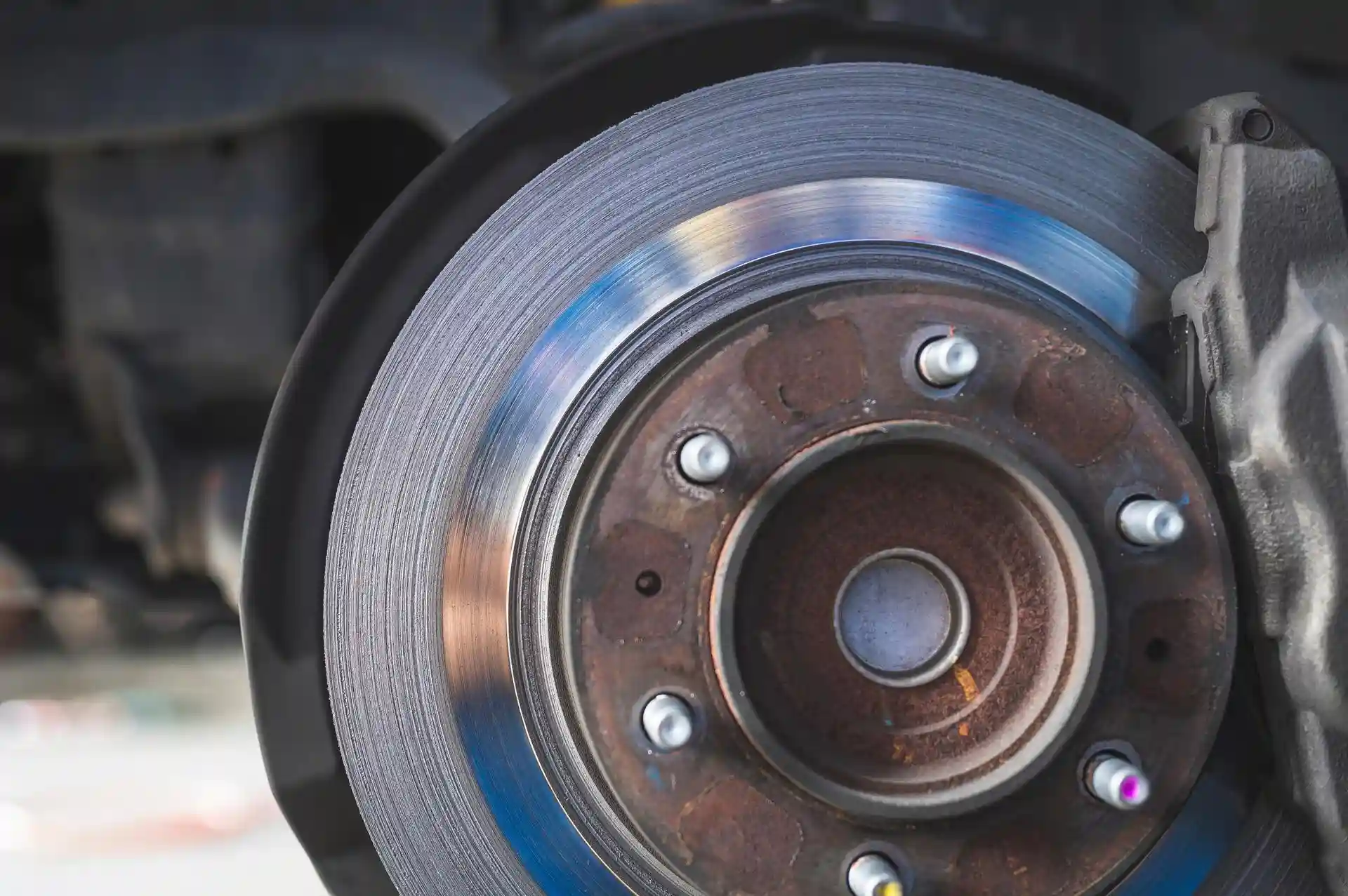 A close-up shot of a heavily grooved and rusted car brake rotor, showing the significant wear and damage caused by worn-out brake pads.